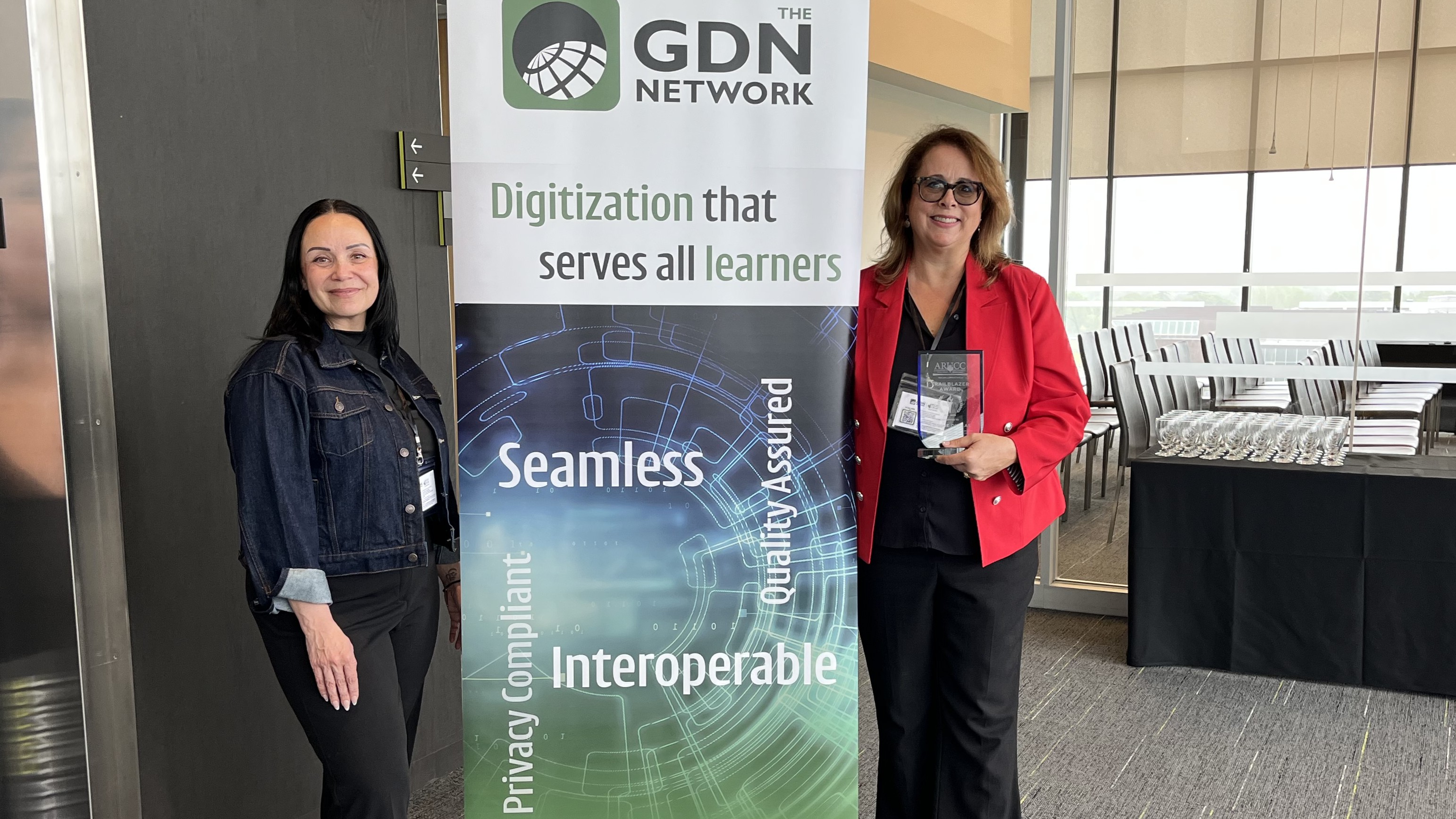 Joanne Duklas, award recipient, standing with Jodi Tavares, MyCreds Executive Direct in front of GDN Network banner